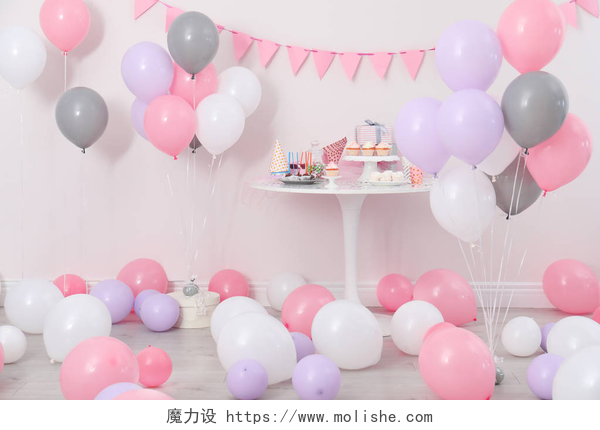 在粉色背景墙的室内有好多种不同颜色的气球在用气球装饰的房间里, 聚会和桌子上的物品